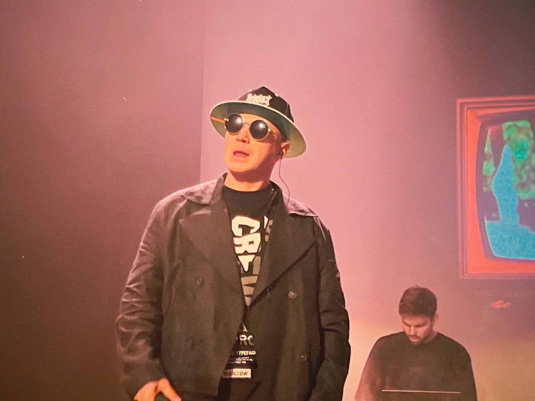 Male artist wearing sunglasses and a hat under warm pink stage lighting