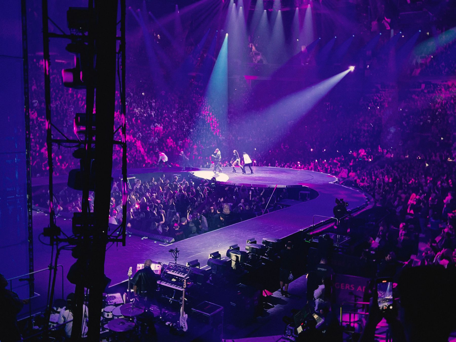 Arena concert photographed from the backstage wings under violet lighting