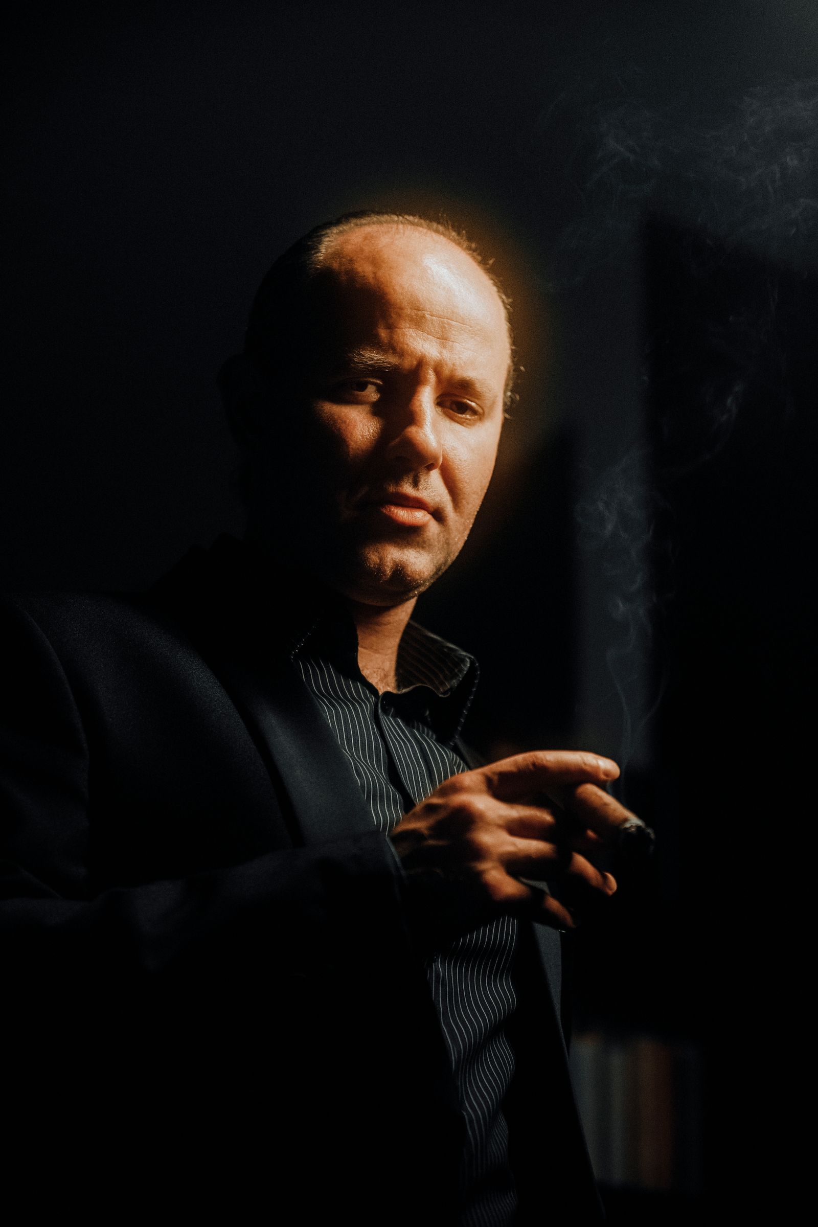 Dramatic editorial portrait of a man in a suit against a black background