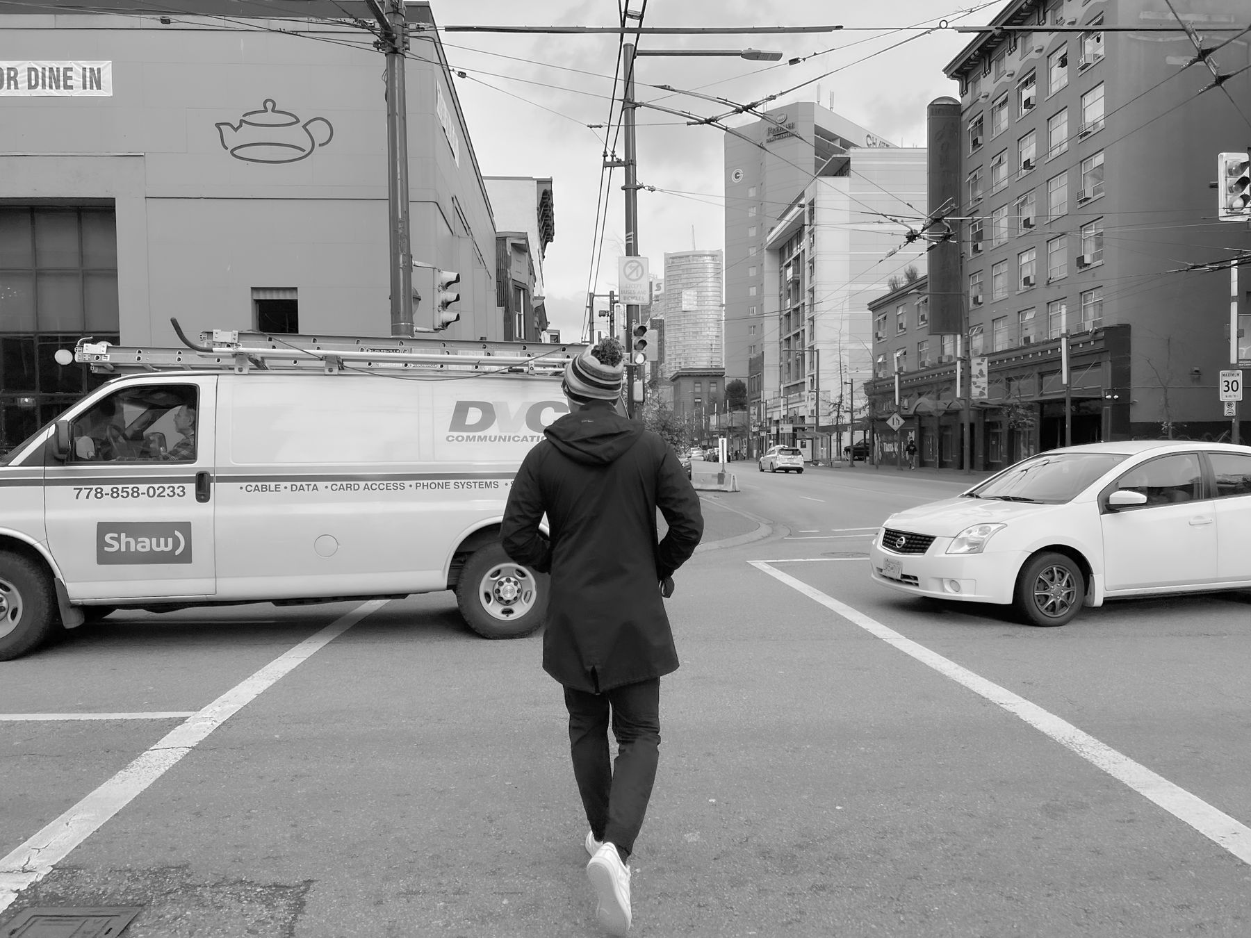 Black-and-white street photograph of a pedestrian crossing a Vancouver intersection